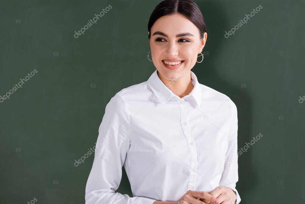 Young teacher in white shirt smiling near chalkboard 