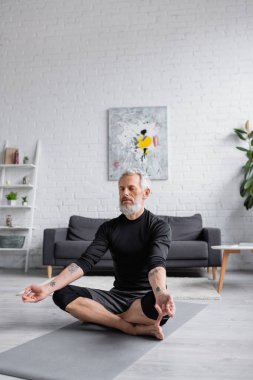 Gözleri kapalı sakallı adam halterin yanındaki yoga minderinde meditasyon yapıyor. 