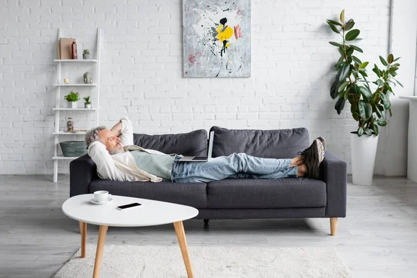 Hombre Barbudo Alegre Mirando Ordenador Portátil Mientras Descansa Sofá — Foto de Stock