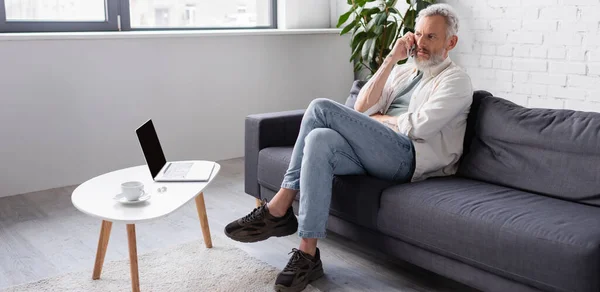 Hombre Barbudo Hablando Teléfono Inteligente Mientras Está Sentado Sofá Cerca — Foto de Stock