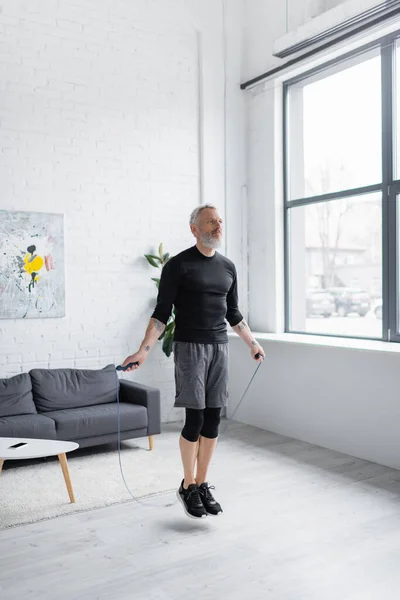 长胡子男子穿着运动服在客厅里用跳绳进行运动 — 图库照片