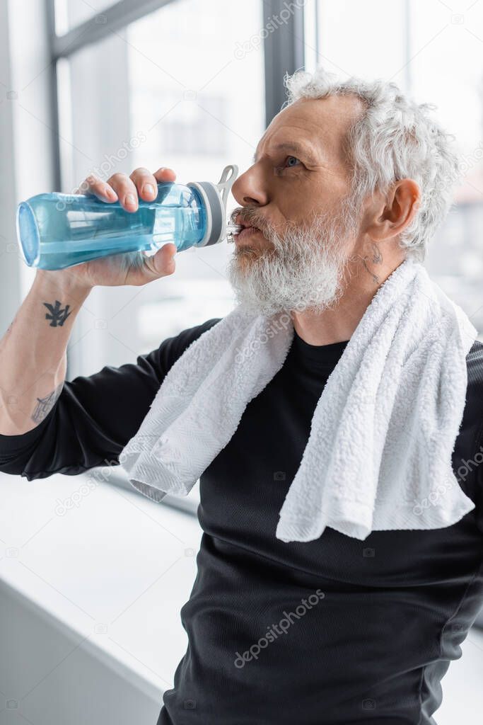 bearded man with grey hair drinking water from sports bottle 