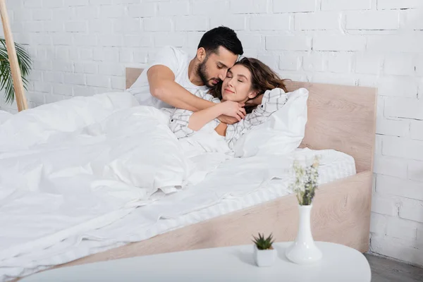 Sorrindo Casal Multiétnico Com Olhos Fechados Abraçando Deitado Cama — Fotografia de Stock