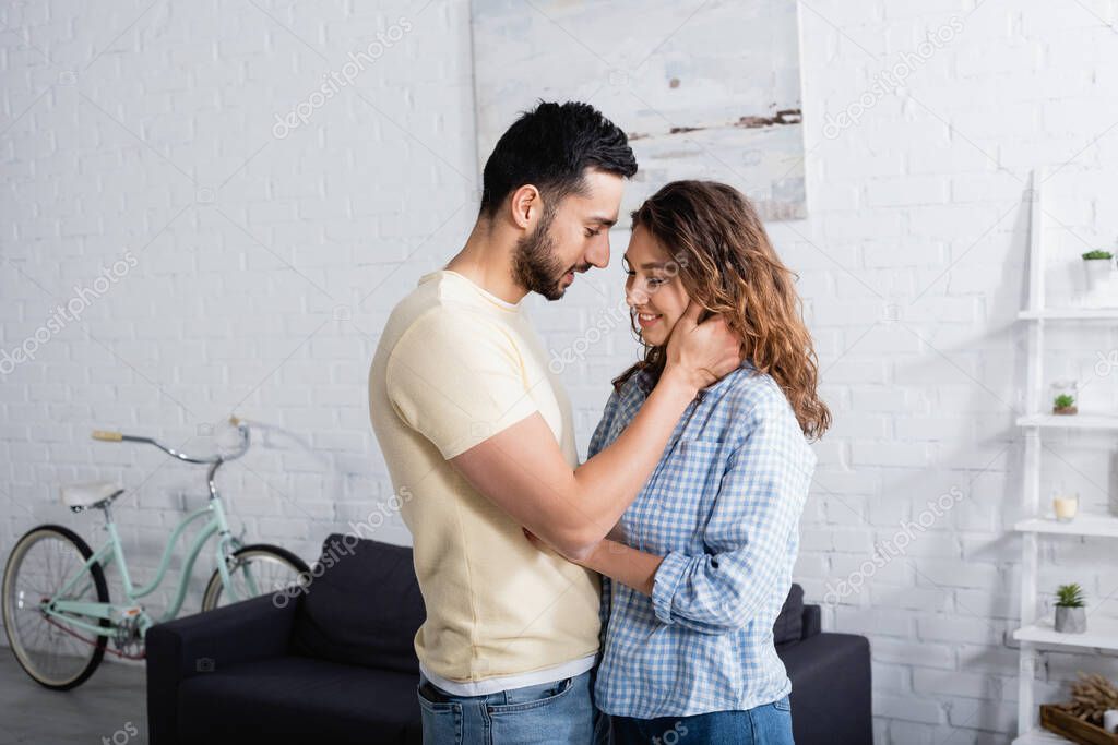 smiling multiethnic man and woman hugging at home