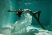 bosá žena v bílých elegantních šatech plavání v bazénu 