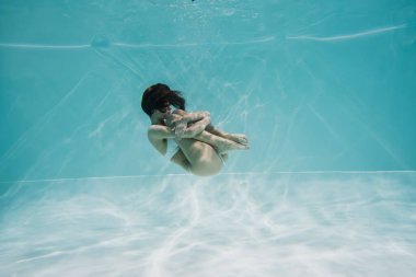 Beyaz mayo giymiş barışçıl esmer kadın havuzda yüzüyor. 