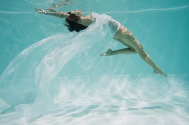 Havuzda yüzen beyaz elbiseli zarif genç kadın. 