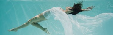Beyaz elbiseli zarif genç bir kadın havuzda yüzüyor. 