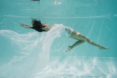Havuzda yüzen beyaz elbiseli zarif bir kadın. 