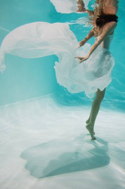Beyaz elbiseli, havuzda yüzen genç bir kadın. 