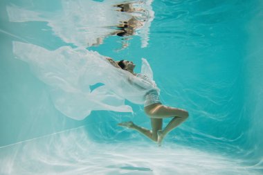 Mavi suyla havuzda yüzen elbiseli genç bir kadın. 