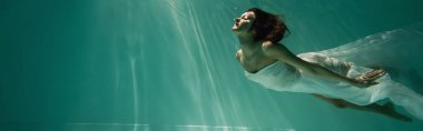 Esmer, genç bir kadın havuza dalıyor, pankartta