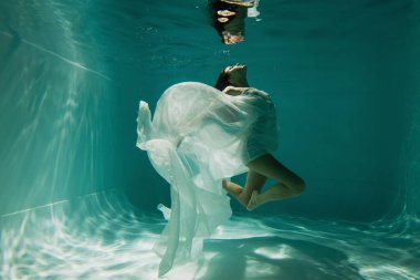 Havuzda yüzen, beyaz, zarif elbiseli, barışçıl genç kadın. 