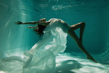 Beyaz, zarif elbiseli, havuzda yüzen çıplak ayaklı kadın. 