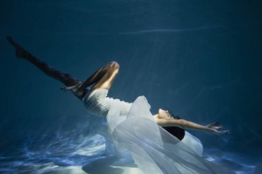 Beyaz elbiseli genç bayanı aydınlatmak mavi suyla havuza dalmak 