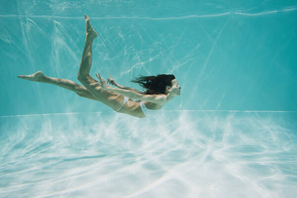 brunette woman in white swimsuit diving in swimming pool 