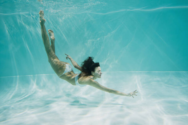 graceful woman in white swimsuit diving in swimming pool 