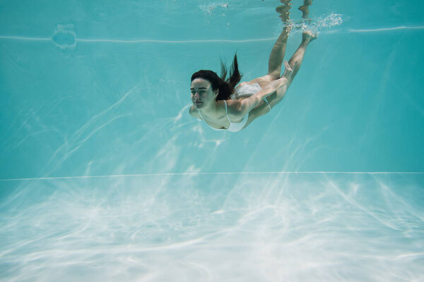 young woman in white swimsuit diving in pool 