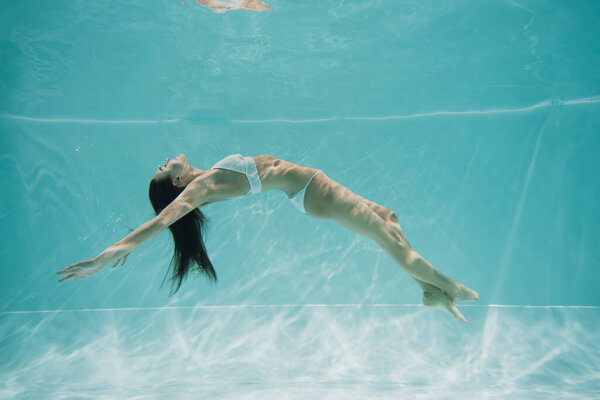 peaceful young woman in white swimsuit swimming in pool 