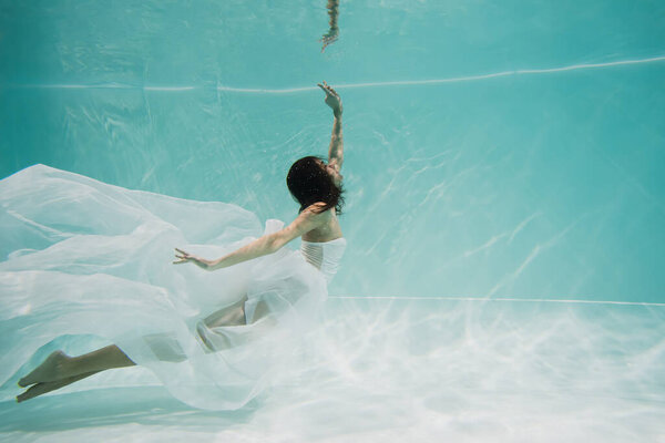 elegant young woman in white dress swimming in pool 
