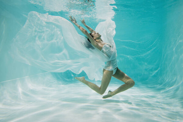 грациозная молодая женщина в белом платье ныряя в бассейне 