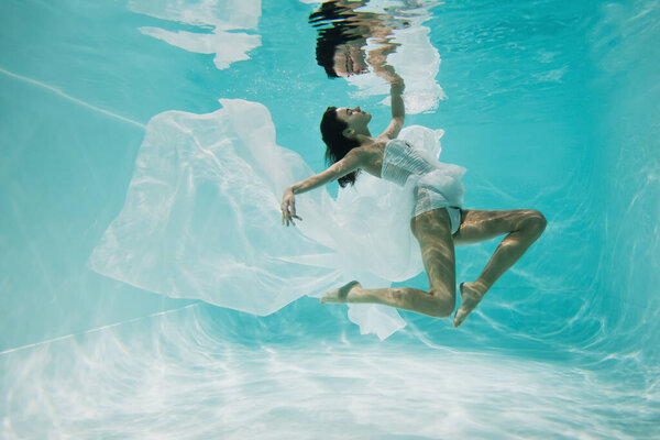 graceful young woman in dress swimming in pool with blue water 