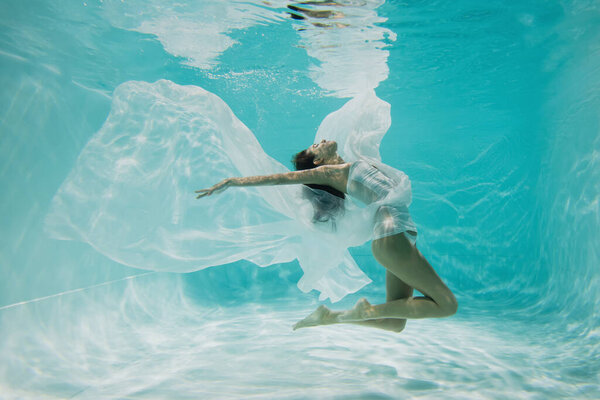 graceful woman in dress swimming in pool with blue water 
