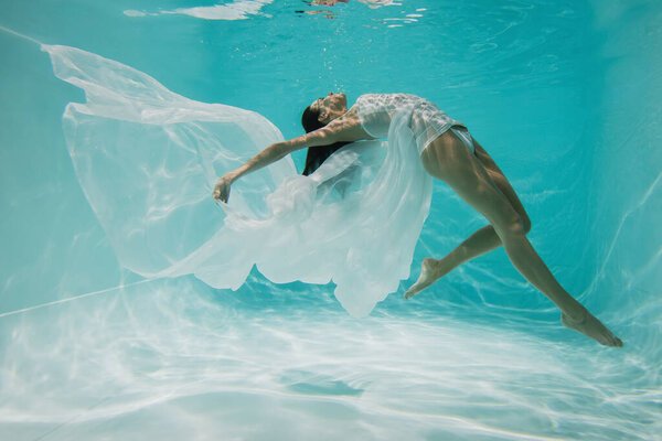 barefoot young woman in dress diving in pool with blue water 