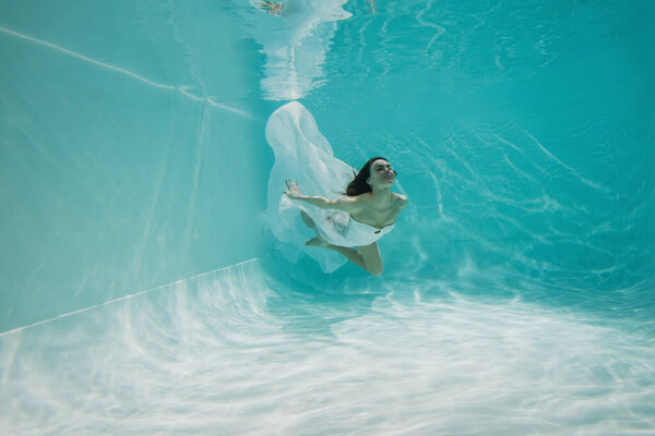 pretty young woman in dress swimming in pool with blue water 