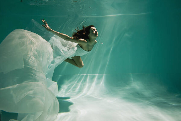 brunette young woman in dress swimming in pool with blue water 