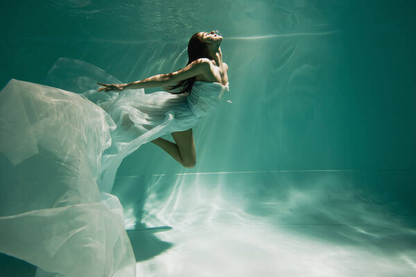 brunette young woman in dress diving in pool 