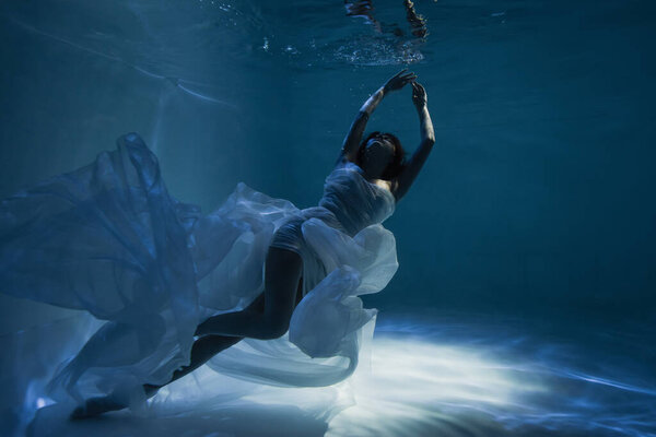 lighting on peaceful woman in white elegant dress swimming in pool 