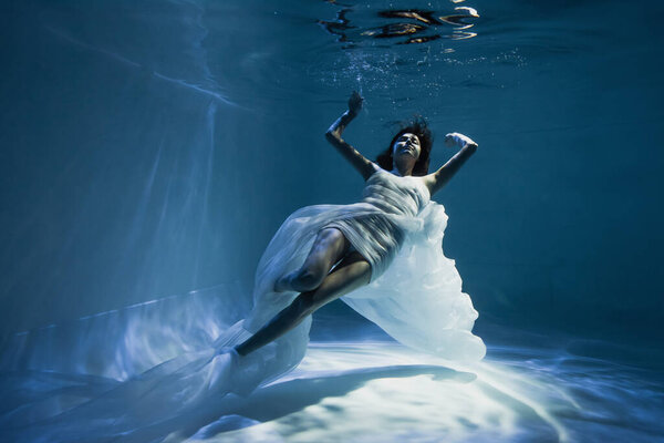 освещение на молодую женщину в белом элегантном платье плавание в бассейне 
