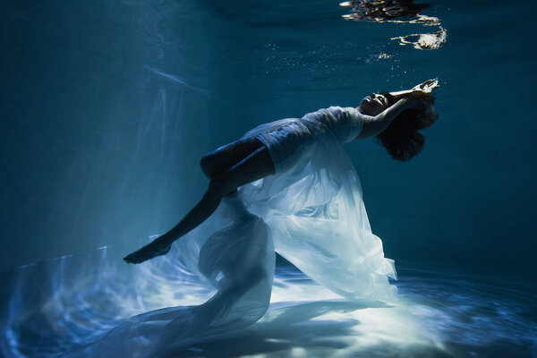 lighting on graceful young woman in white elegant dress swimming in pool 