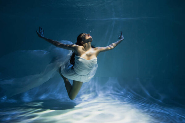 lighting on young woman in white dress diving in swimming pool 