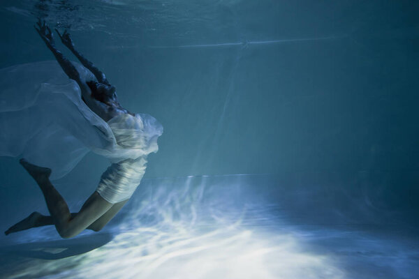 lighting near young graceful woman in white elegant dress swimming in pool with blue water 