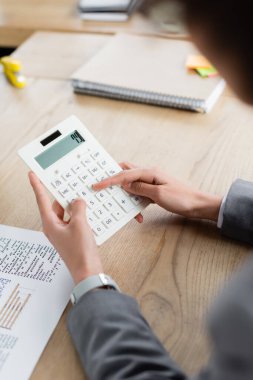 Belge yanında hesap makinesi kullanan iş kadınının kırpılmış görünümü ve bulanık defter 
