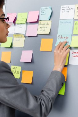 Blurred african american businesswoman looking at colorful sticky notes with lettering  clipart