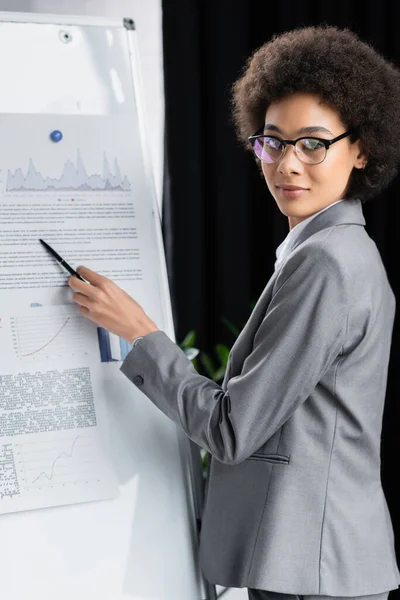 Afroamerikanische Geschäftsfrau Blickt Kamera Und Zeigt Auf Verschwommenes Flipchart — Stockfoto