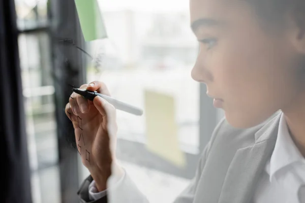 Marker in hand of blurred african american manager writing on glass board in office