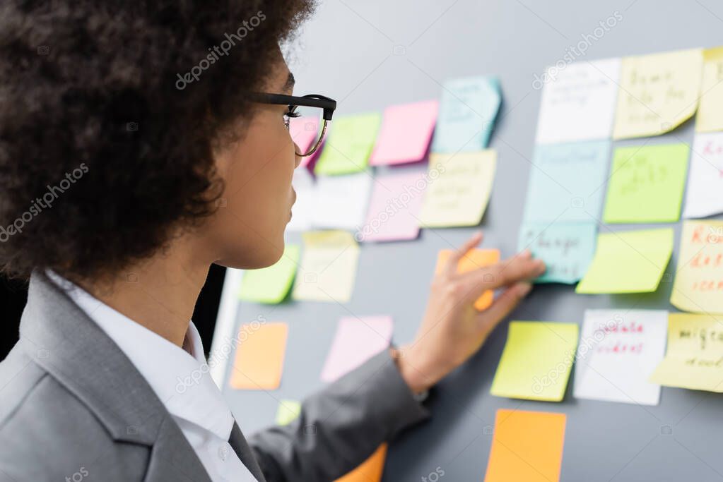African american businesswoman standing near flipchart with sticky notes on blurred background 