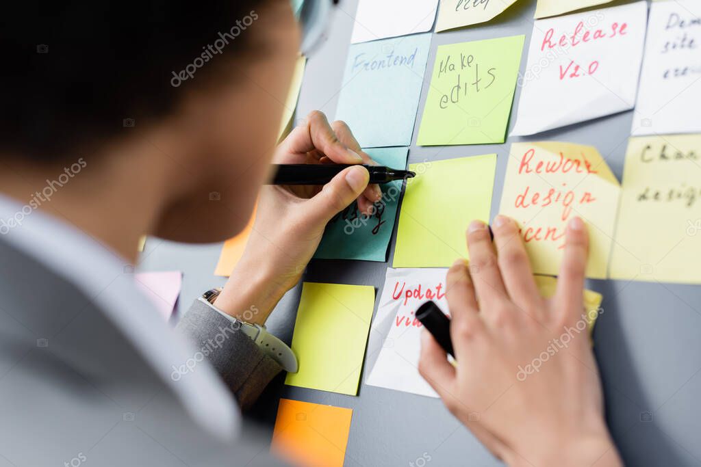 Cropped view of blurred african american businesswoman writing on sticky note 