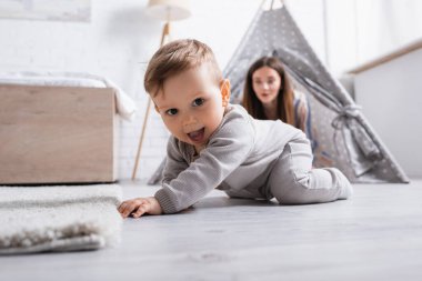 excited baby boy crawling on floor near mother on blurred background  clipart