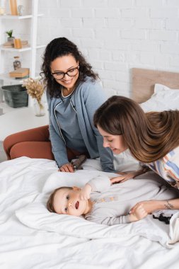 Mutlu dövmeli anne, neşeli Afro-Amerikan bir kadının yanında yatan küçük çocuğa bakıyor.