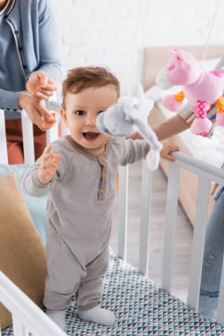Bebek karyolasında heyecanlı bebek çocuk Bulanık ön planda yumuşak oyuncaklar asılı