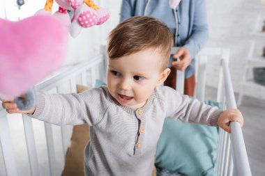 Bebek beşiğinde neşeli bir çocuk Bulanık ön planda yumuşak oyuncaklar asılı