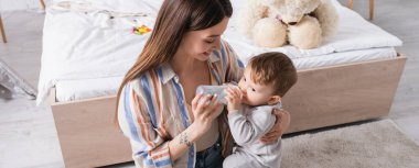 Dövmeli anne bebeğini şişeden sütle besliyor.