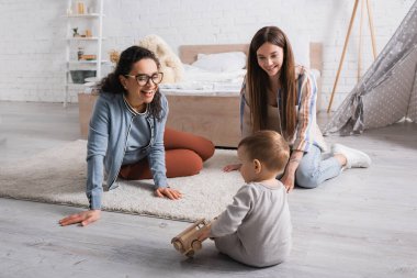 Küçük çocuk tahta oyuncak arabayla oynuyor. Neredeyse çok ırklı kadınları memnun ediyor. 