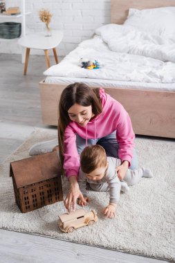 Mutlu anne ve bebek çocuk oyuncak evin yanında tahta arabayla oynuyorlar.