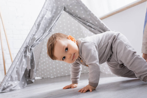 baby boy in romper crawling near tipi at home 